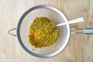 Extracting juice from passion fruits with a strainer and a spoon
