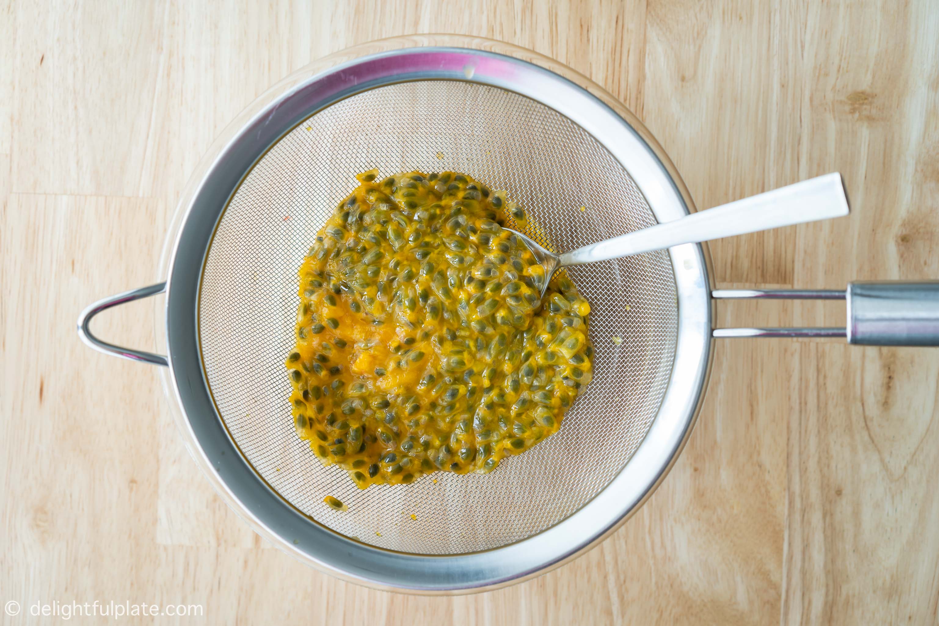 Extracting juice from passion fruits with a strainer and a spoon