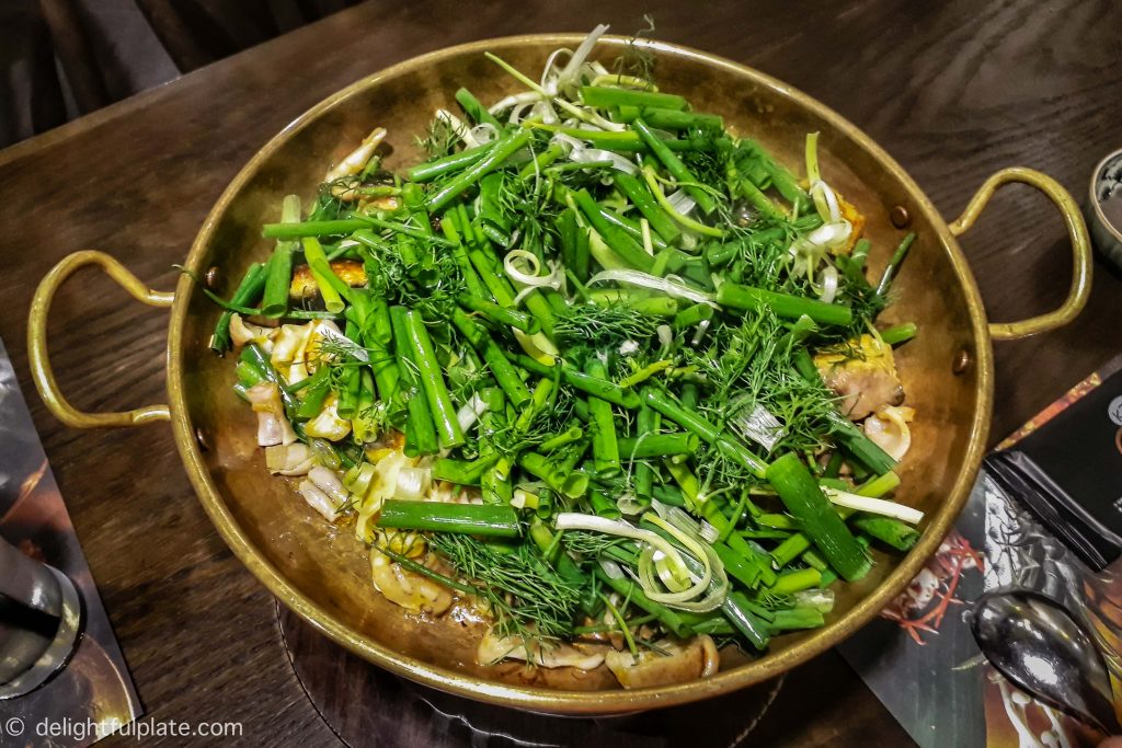 A sizzling pan of cha ca Hanoi with fried fish chunks, spring onion and dill