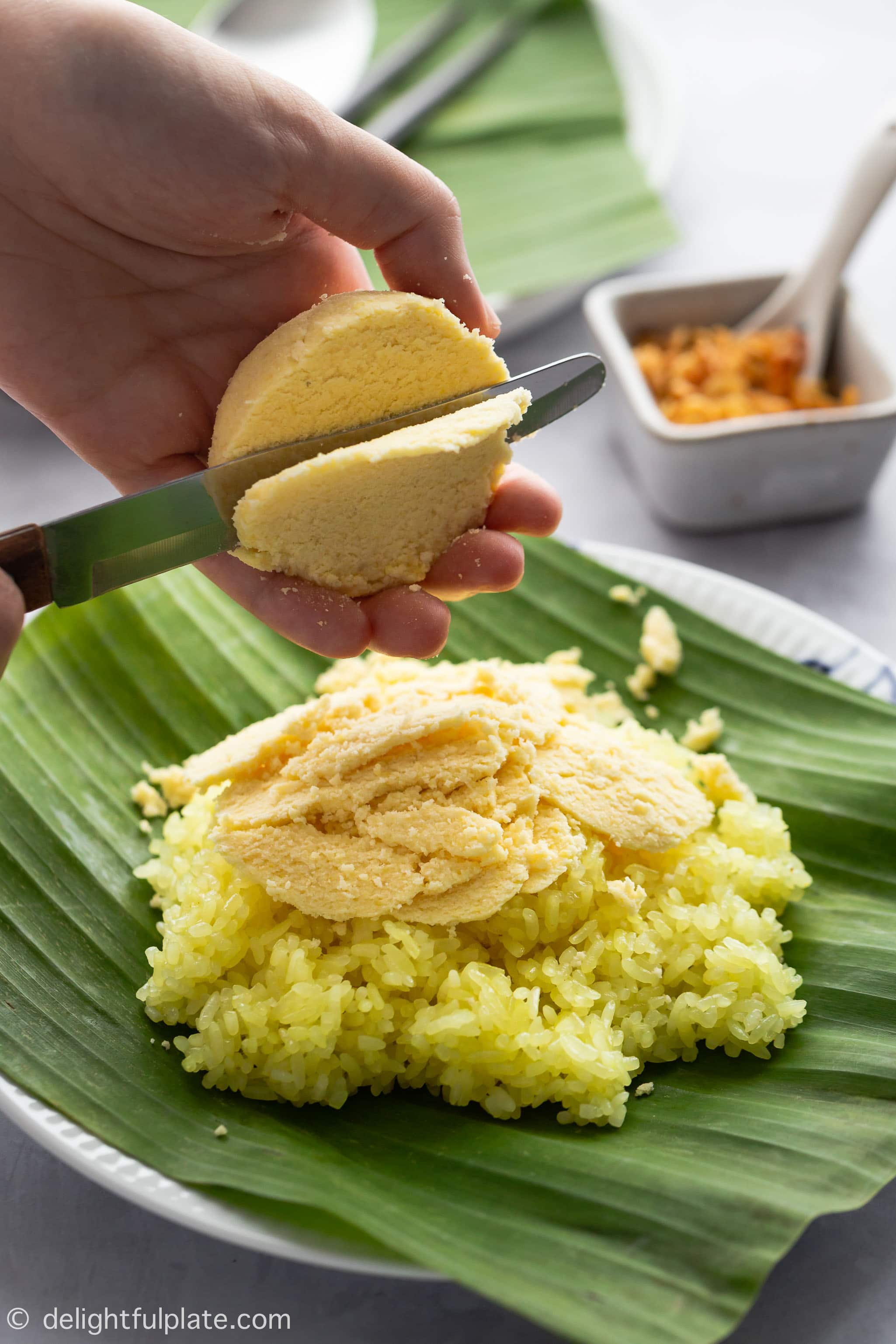 Cutting mung bean balls into thin slices over the steamed sticky rice on the plate.