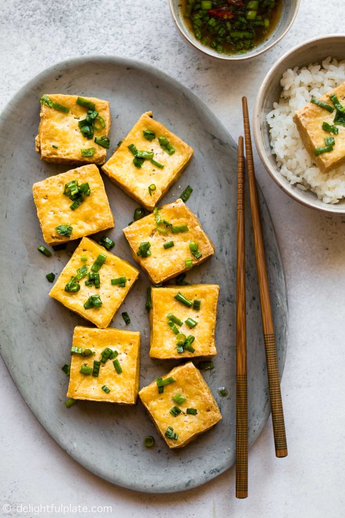 a plate of fried tofu that has been dipped in scallion fish sauce mixture. Serve with a bowl of rice and sauce on the side.