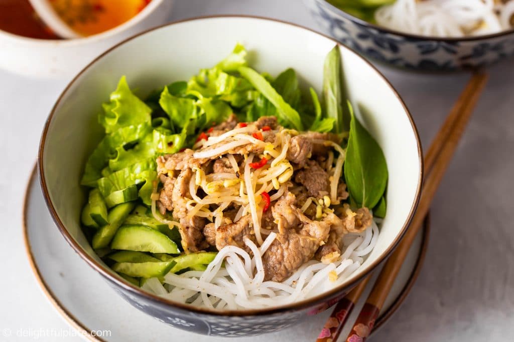 A bowl of Vietnamese lemongrass pork noodle salad (bun this xao) with stir-fried pork, beansprouts, noodles, cucumber, lettuce and herbs.