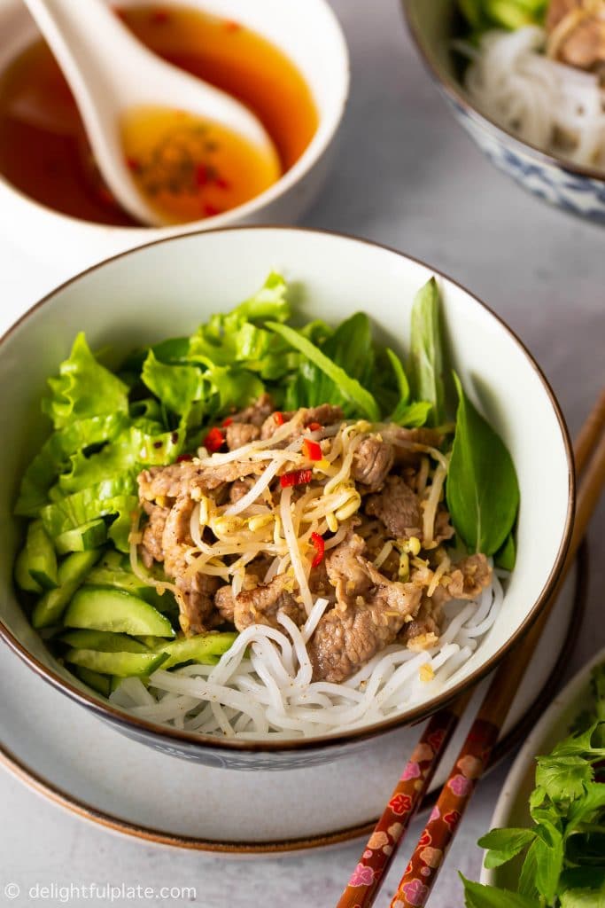 A bowl of Vietnamese lemongrass pork noodle salad (bun this xao) with stir-fried pork, beansprouts, noodles, cucumber, lettuce and herbs. Serve with dressing.