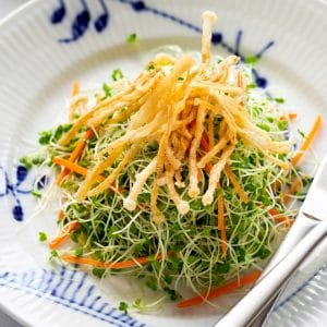 a plate of microgreens salad topped with crispy fried enoki mushrooms