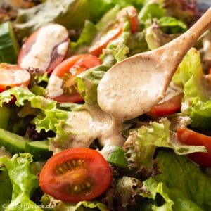 a spoon of sesame dressing being drizzled over green salad