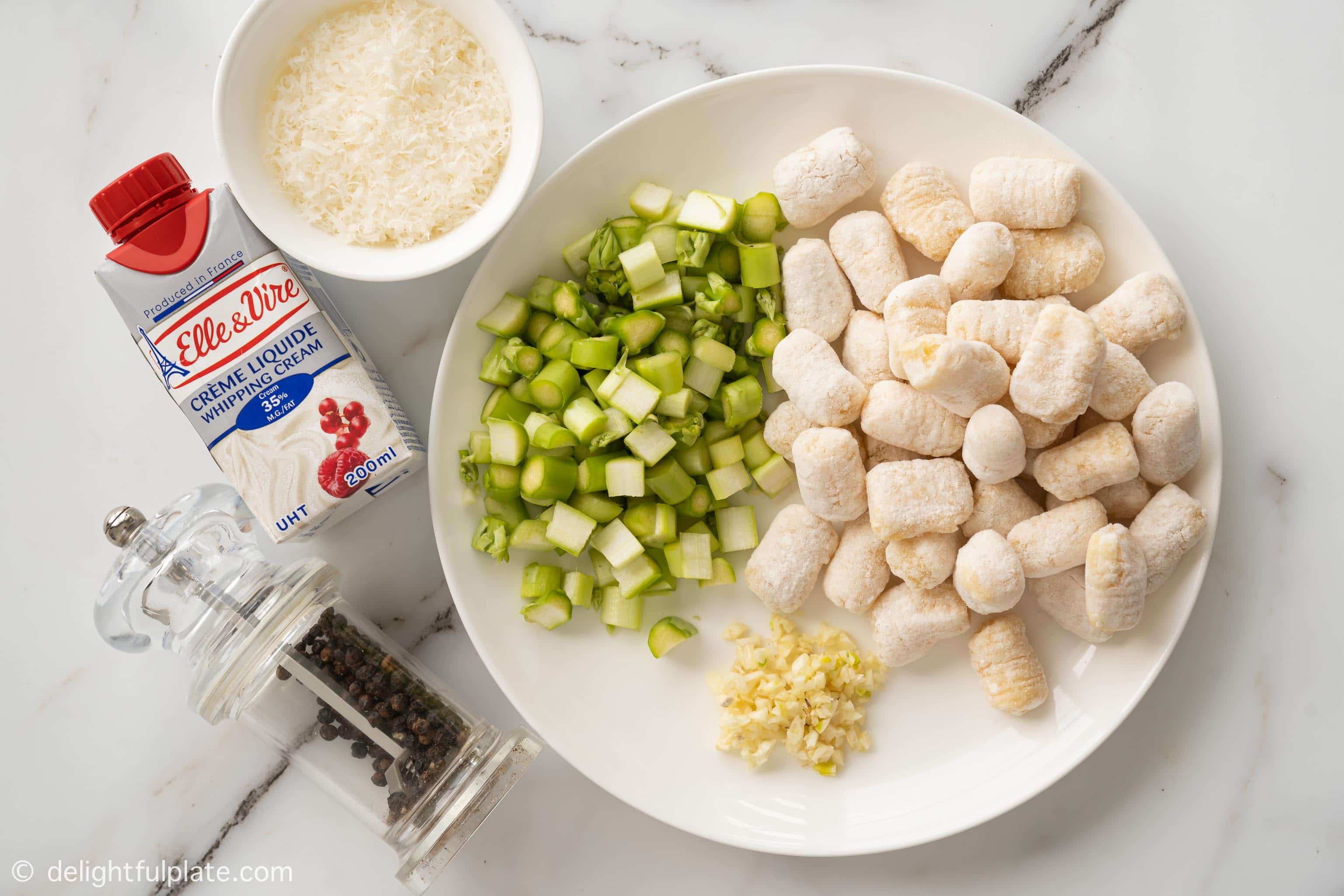 plates and bowls containing ingredients to make the dish: asparagus, gnocchi, garlic, parmesan, cream and black pepper