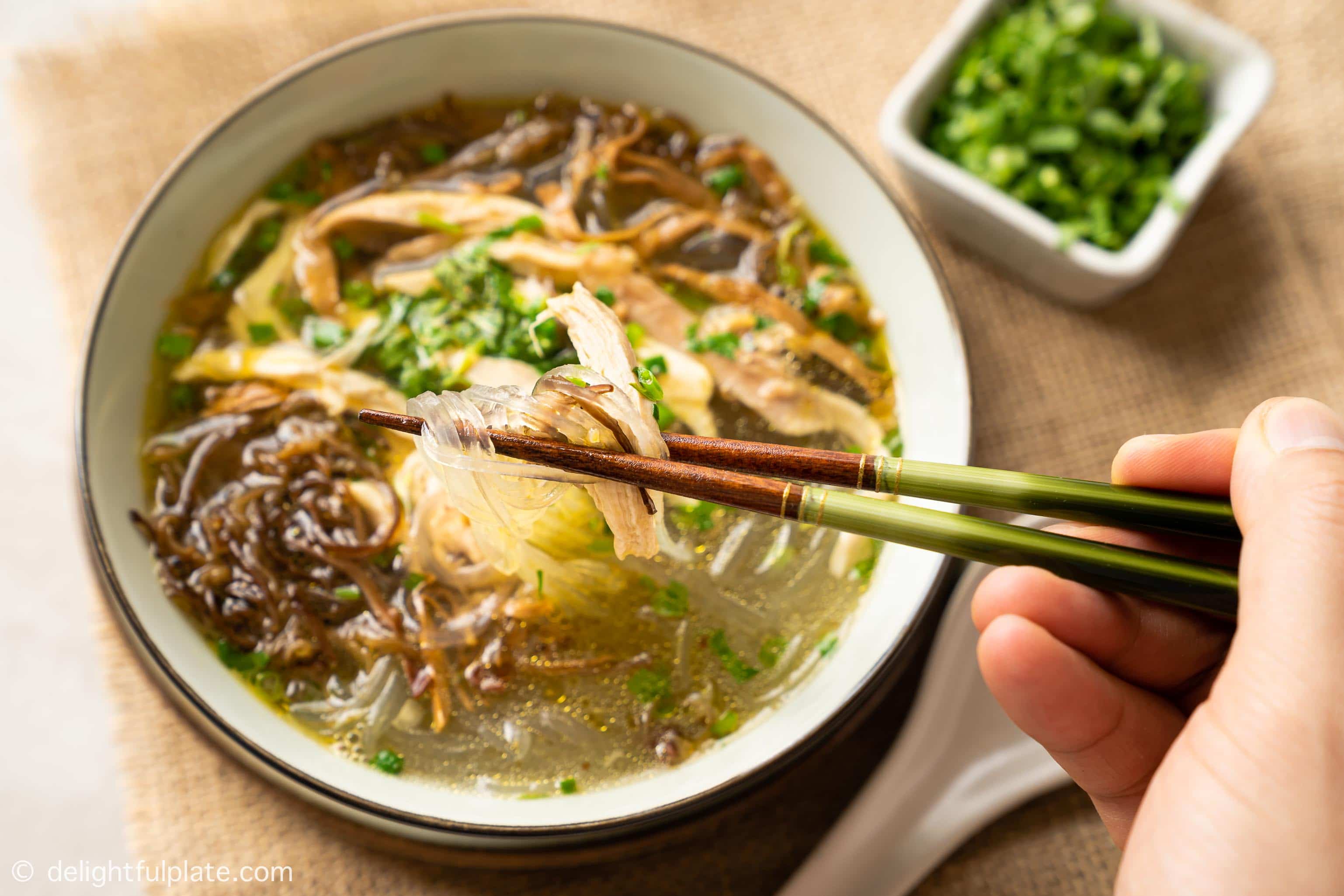 picking up chicken glass noodle soup from a bowl with chopsticks