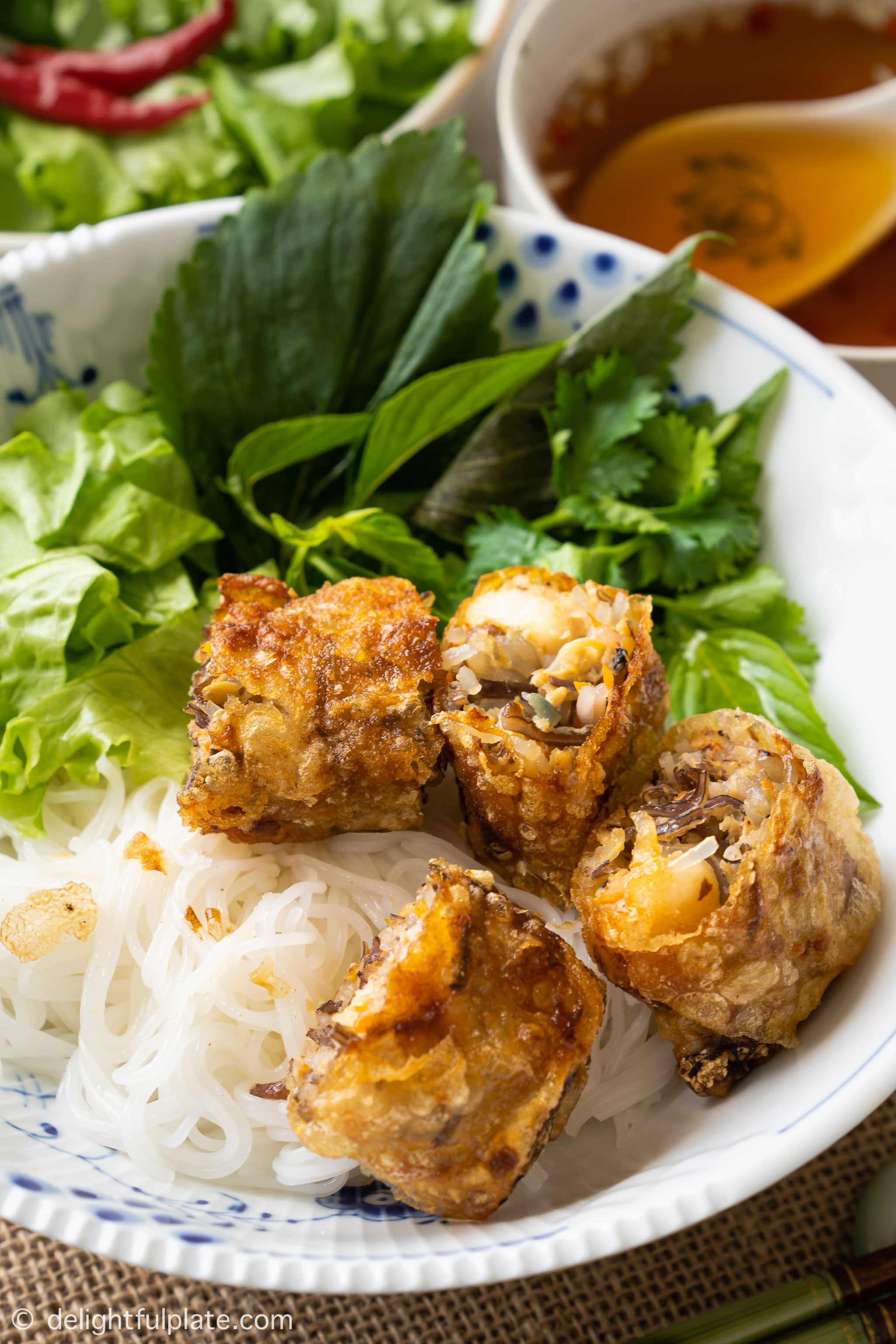a bowl of rice vermicelli noodles, fried spring rolls, lettuce and fresh herbs