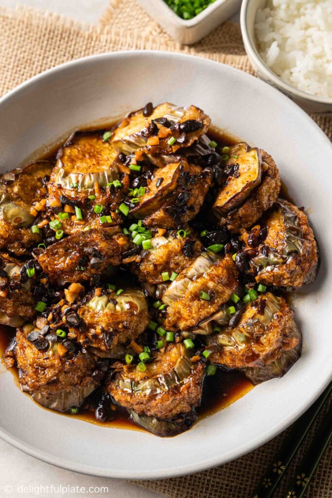 a plate of stuffed eggplant with black bean sauce, served with rice