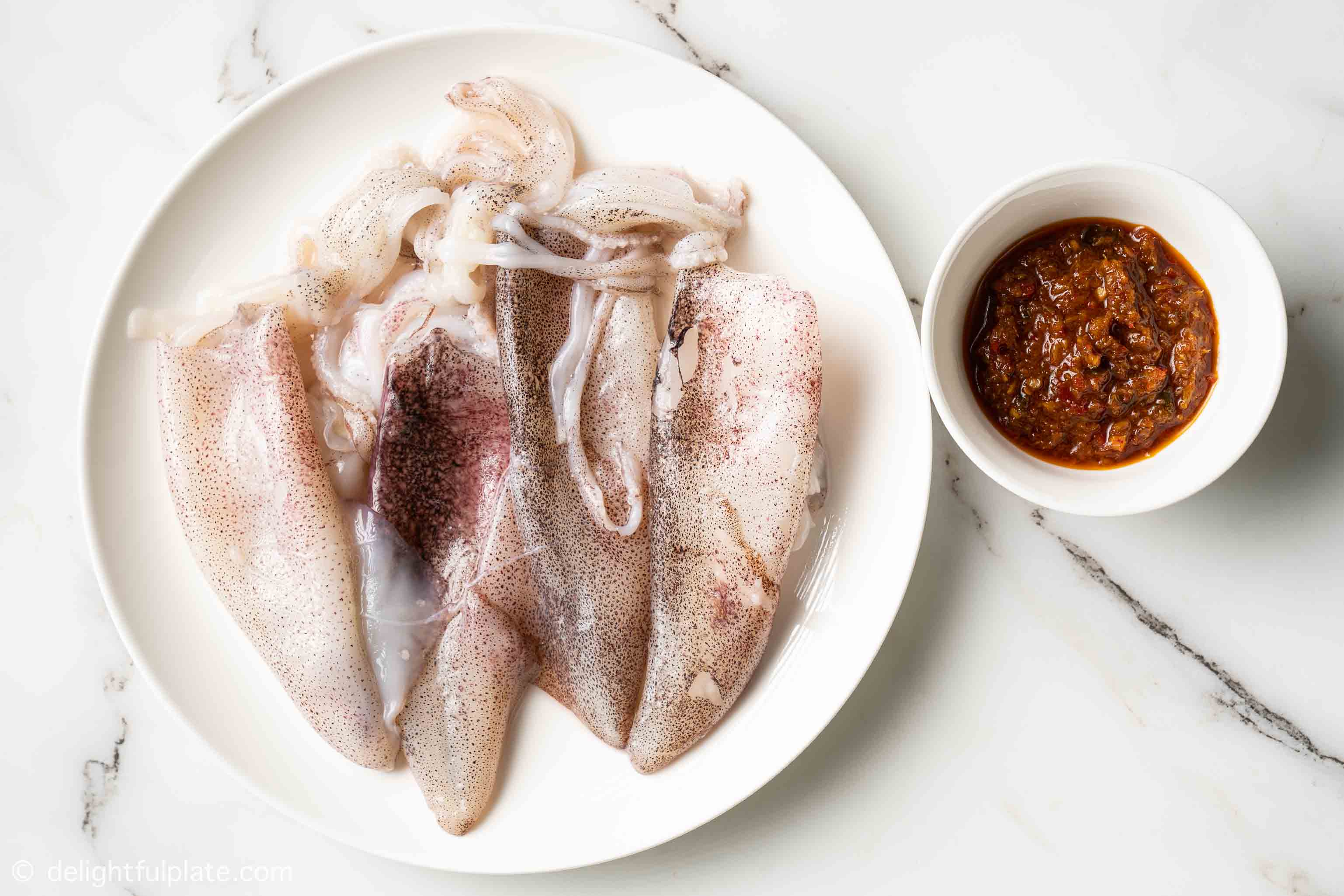 plate and bowl containing squids and sate sauce