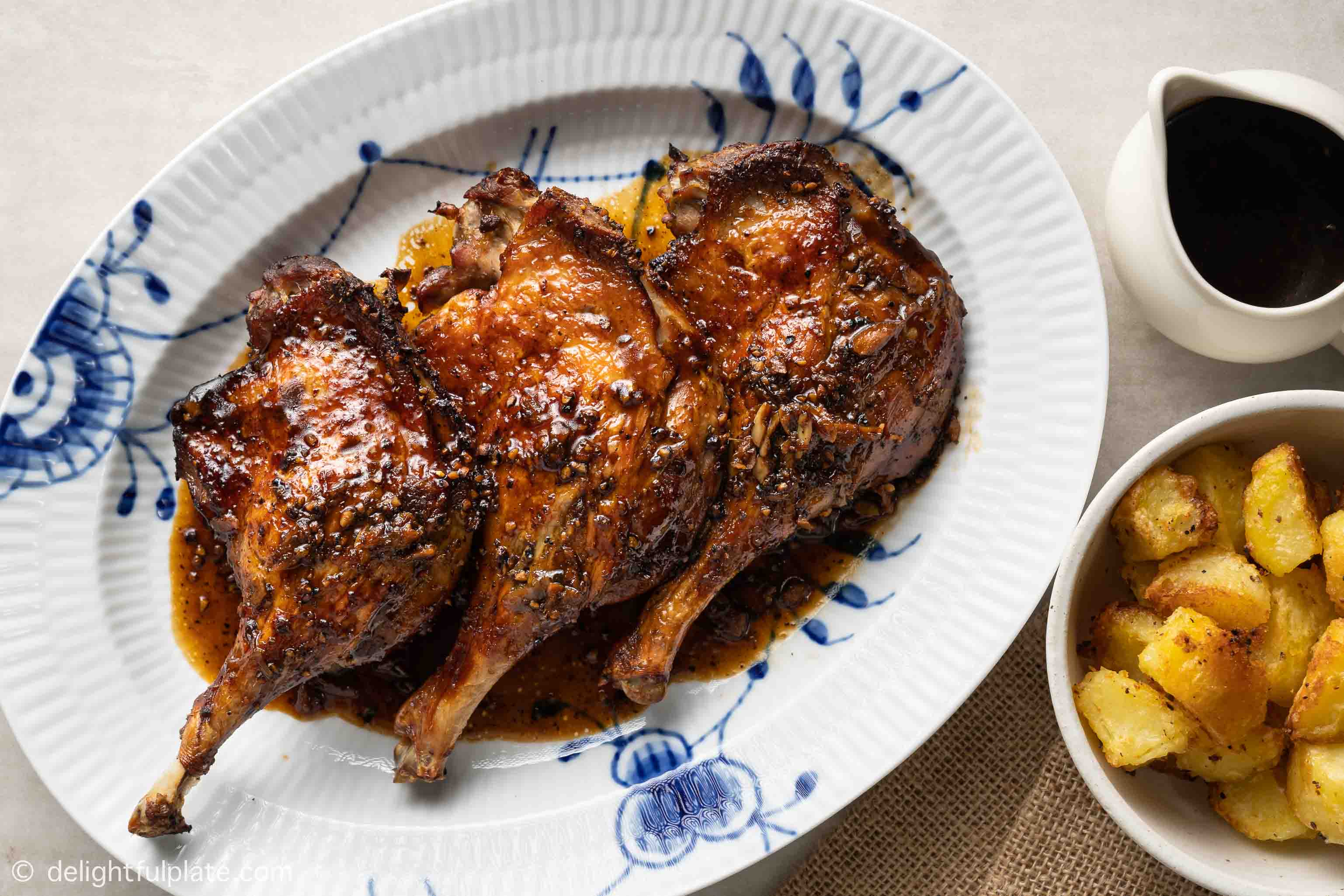 a plate of roasted duck legs served with black pepper sauce and potatoes